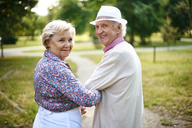 An older couple taking a walk turn behind them to smile at the camera.