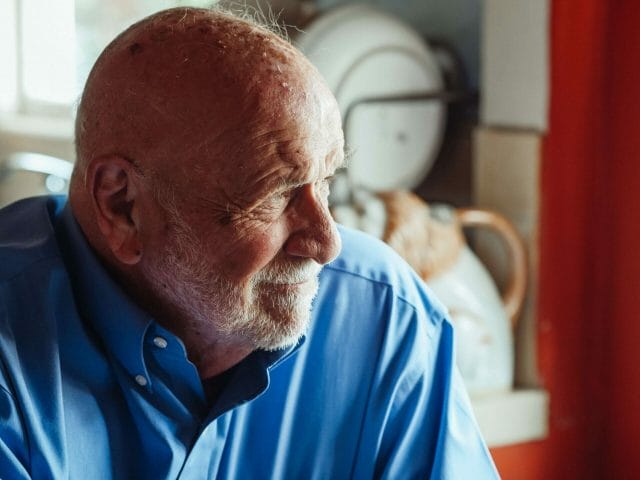 A close-up portrait of an older adult man gazing out a window.