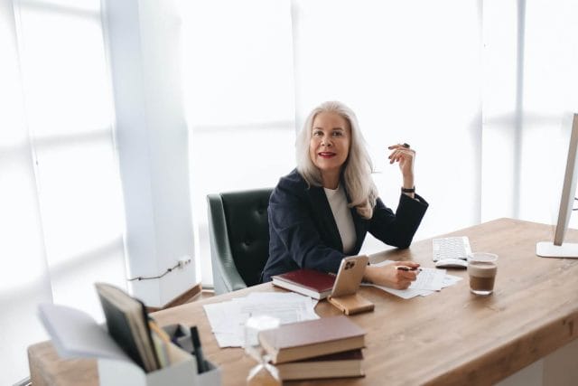 A mature business woman looks up at the camera while working at her desk.