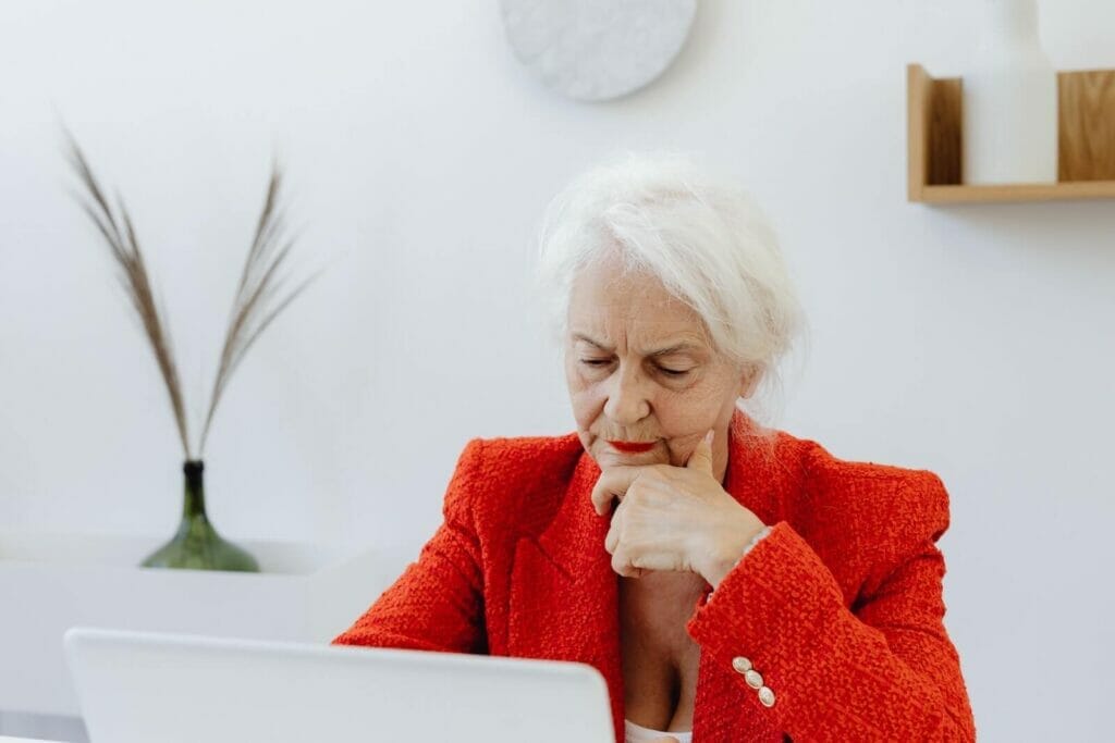 An older adult woman looks seriously at her computer laptop screen.