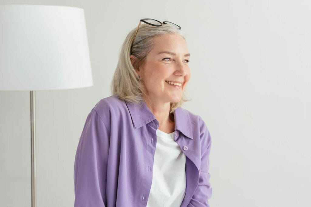 An older adult woman smiles and looks off into the distance.