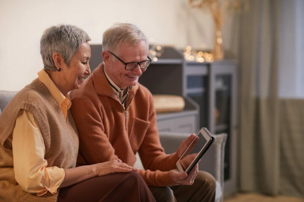 An older adult couple looks at a tablet and smile at what they see.