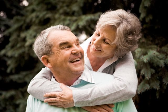 Portrait of senior female embracing her husband while he is laughing and looking at her.