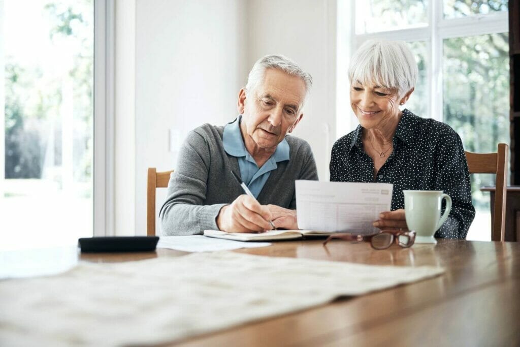 An older adult man and woman sit at a table looking at paperwork.
