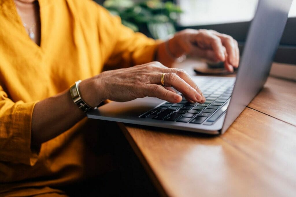 An older adult woman's hands type on a laptop computer.