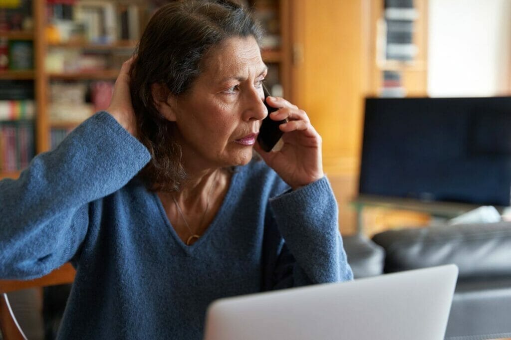 An older adult woman talks on the phone, looking concerned.