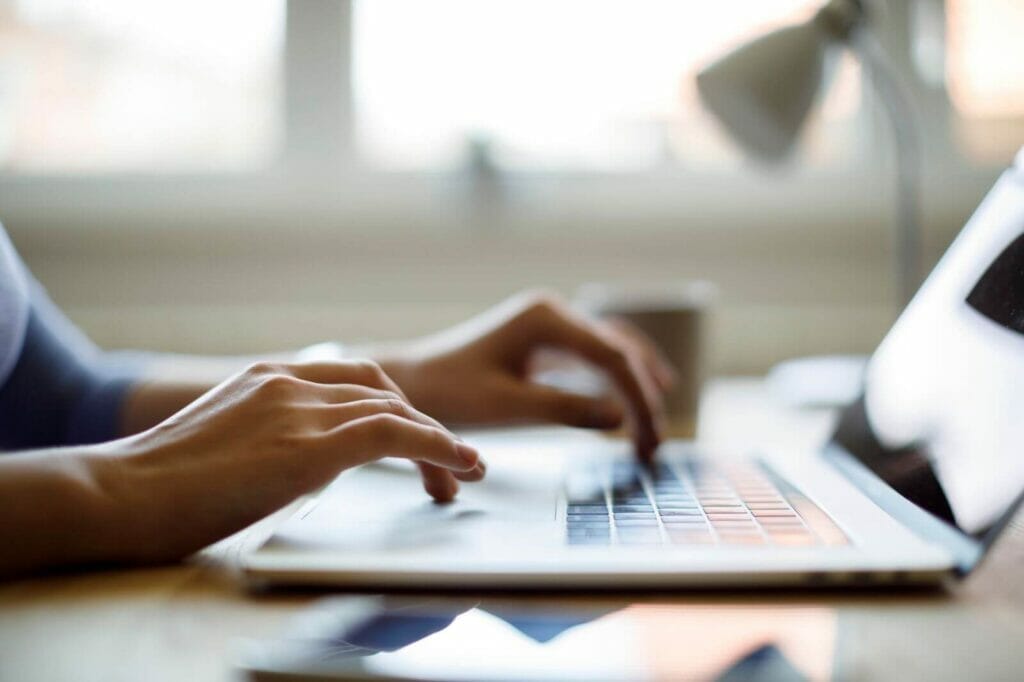 A person's hands type on a laptop computer.