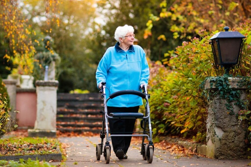 An older adult woman walks outside in the fall using a walker.