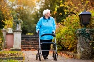 An older adult woman walks outside in the fall using a walker.