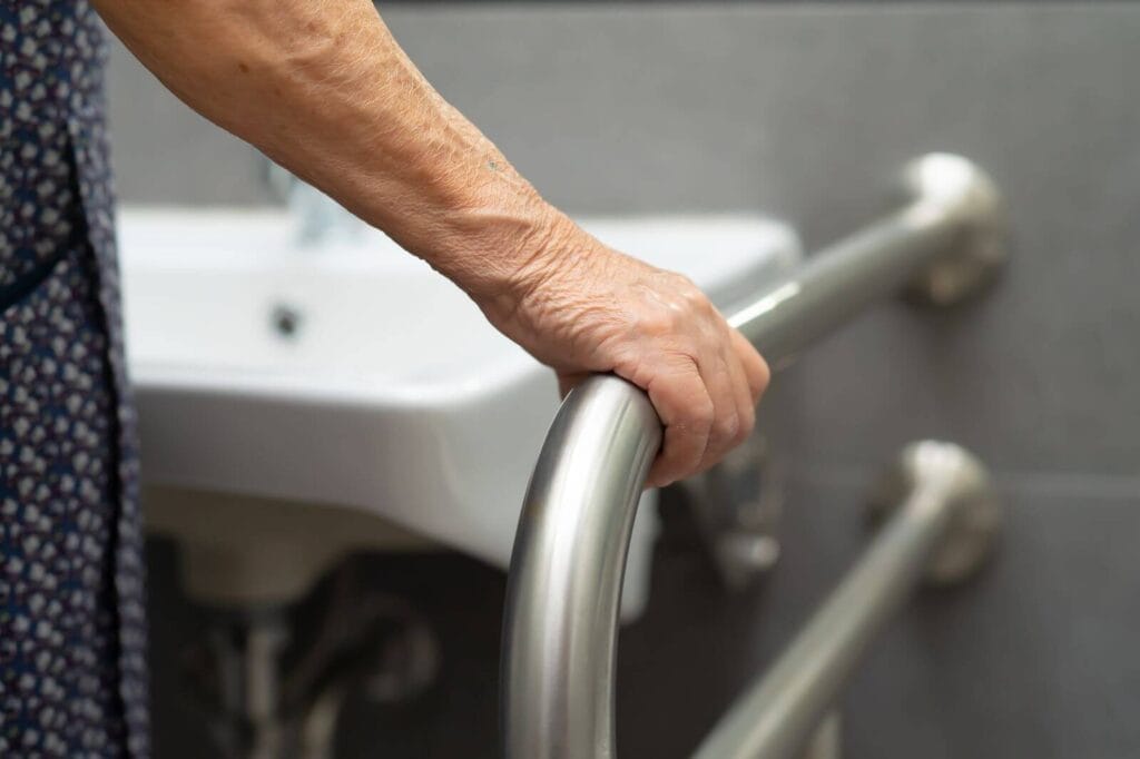 An older adult woman's hand grips a support rail next to a bathroom sink.
