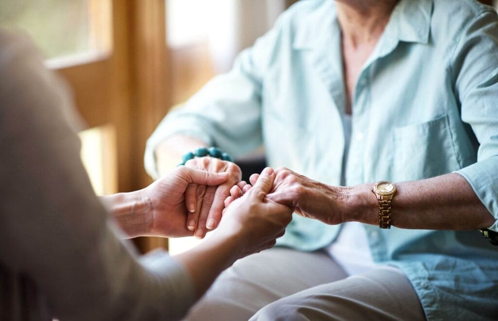 A person holds the hands of an older adult woman.