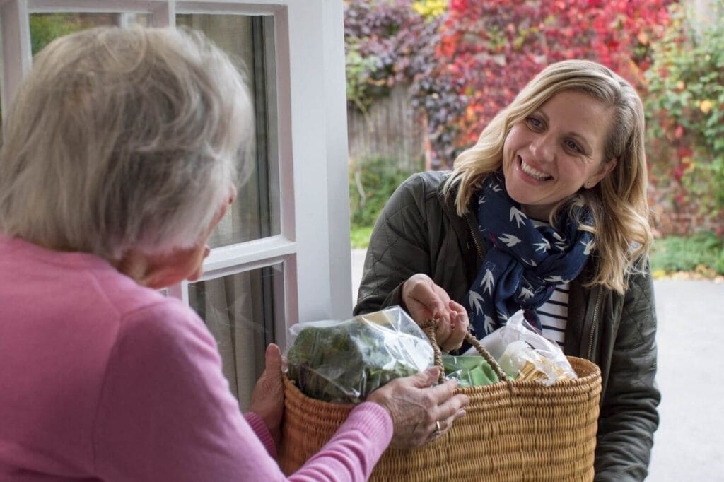 A woman hands a bag of groceries to an older adult woman.