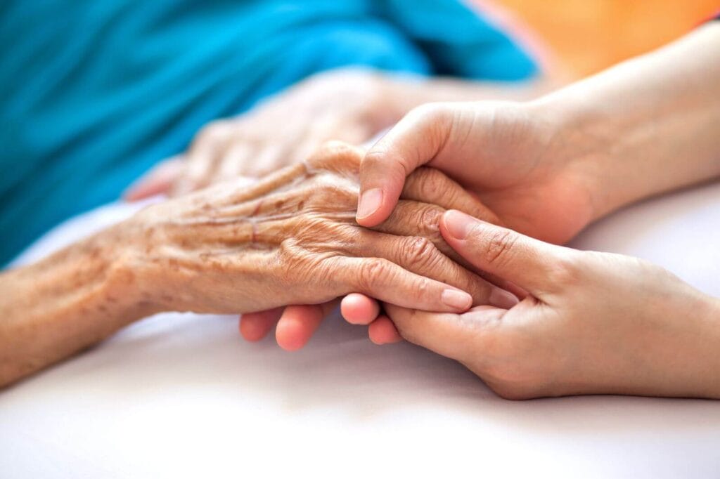 A person holds the hand of an older adult woman.