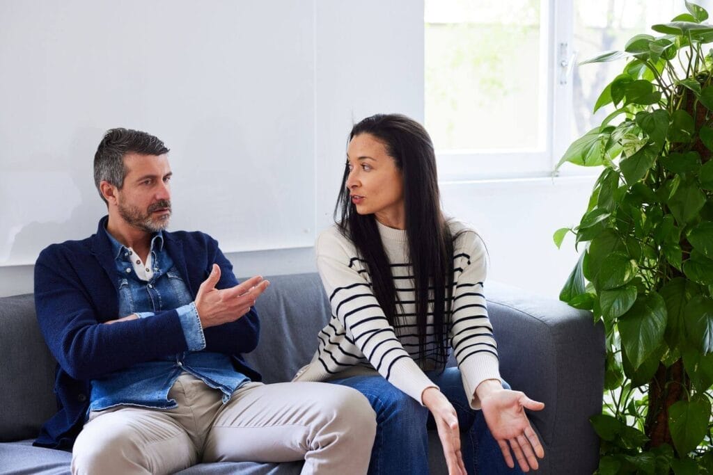 A woman and man sit on a couch having a discussion.