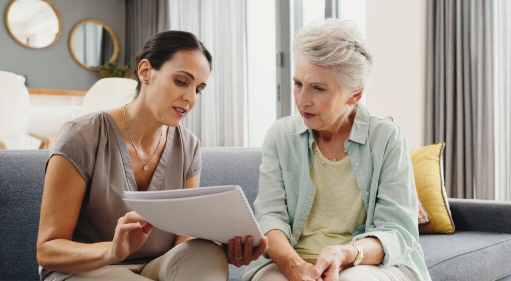 A woman shows a notebook to an older adult woman.