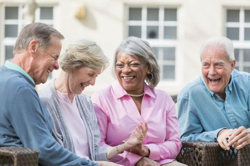 Two older adult men and two older adult women sit together, laughing.