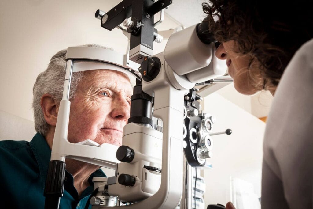 A woman optometrist gives an eye exam to an older adult man.
