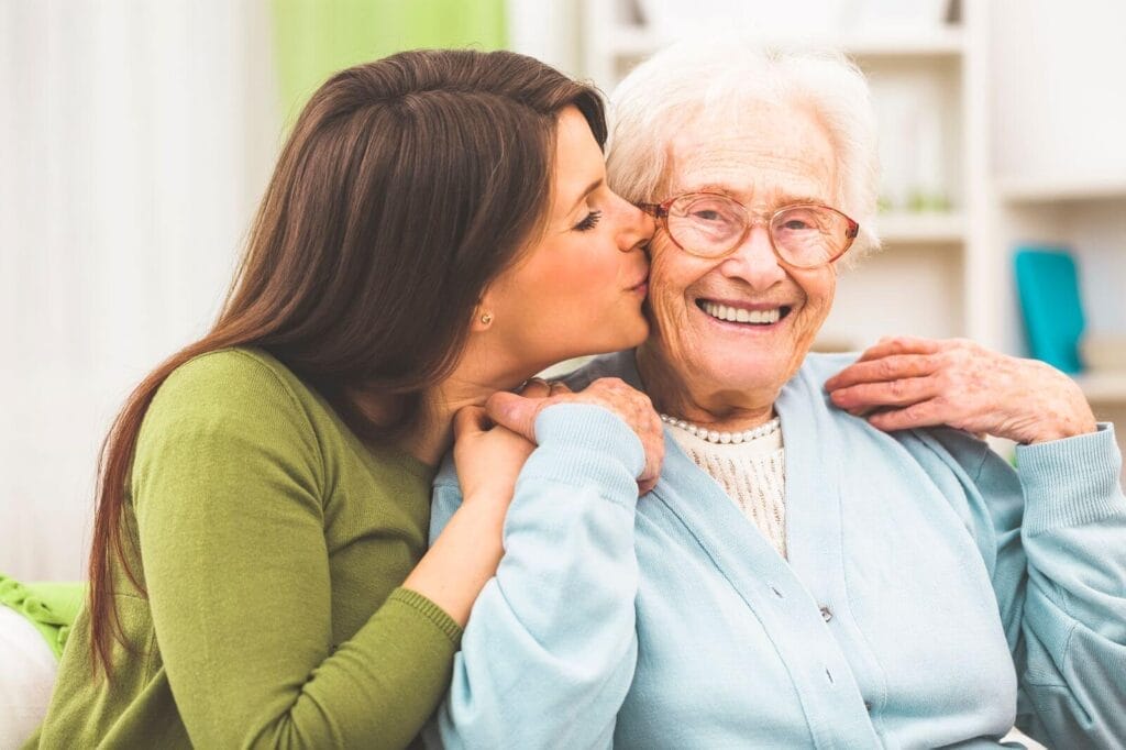 A woman gives an older adult woman a kiss on the cheek.