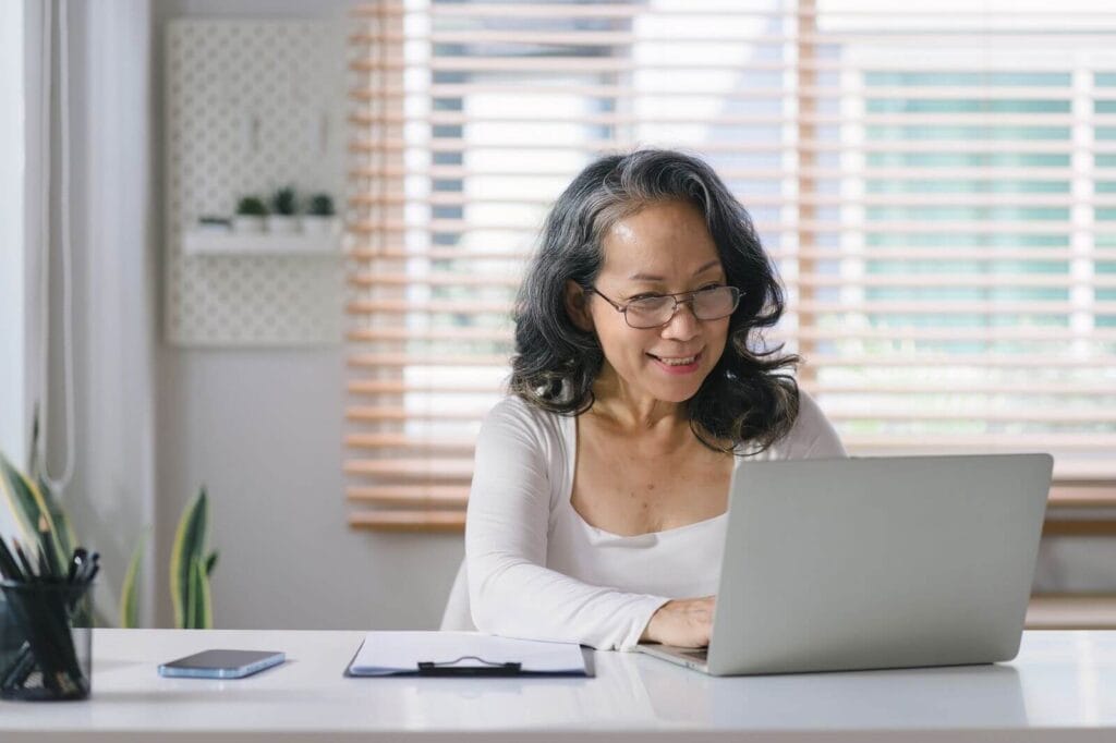 A smiling older adult woman uses her laptop computer.