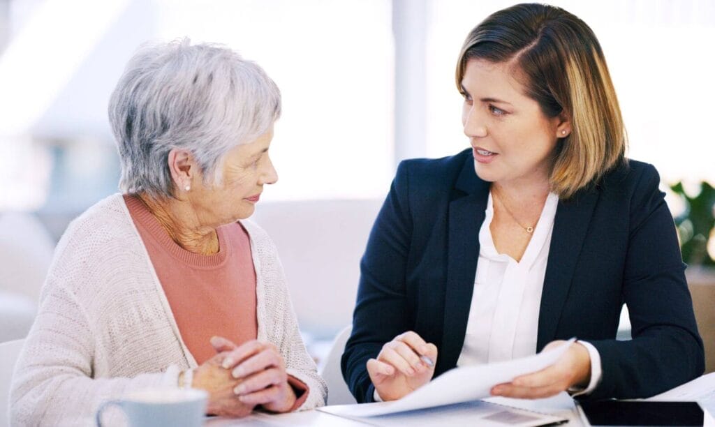A woman and an older adult woman sit at a table discussing paperwork.