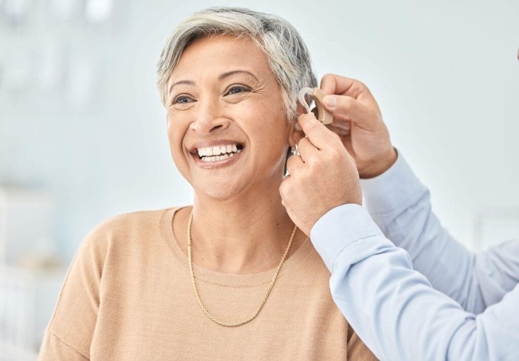 A person places a hearing aid on an older adult woman's ear.