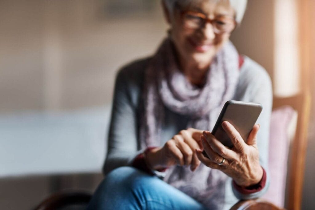 An older adult woman looks down at her cell phone, smiling.