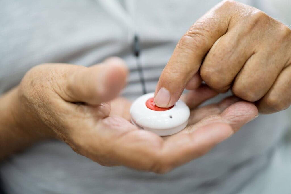 An older adult man's hand presses the button on his medical alert system pendant.