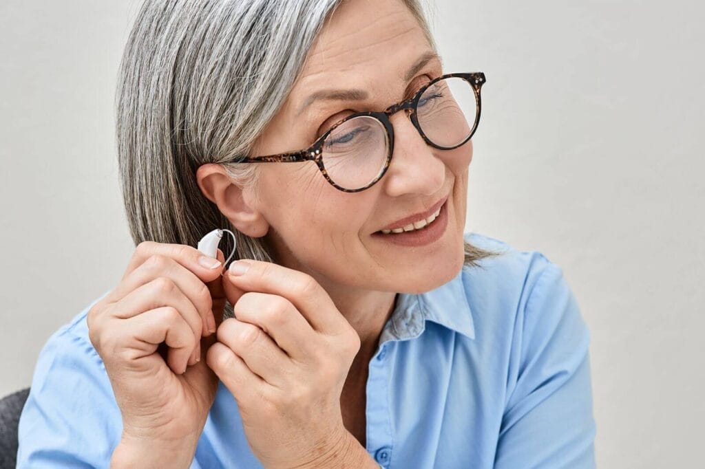 An older adult woman is getting ready to place a hearing aid in her ear.