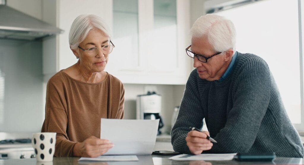 An older adult man and woman sit at a table looking over paperwork.