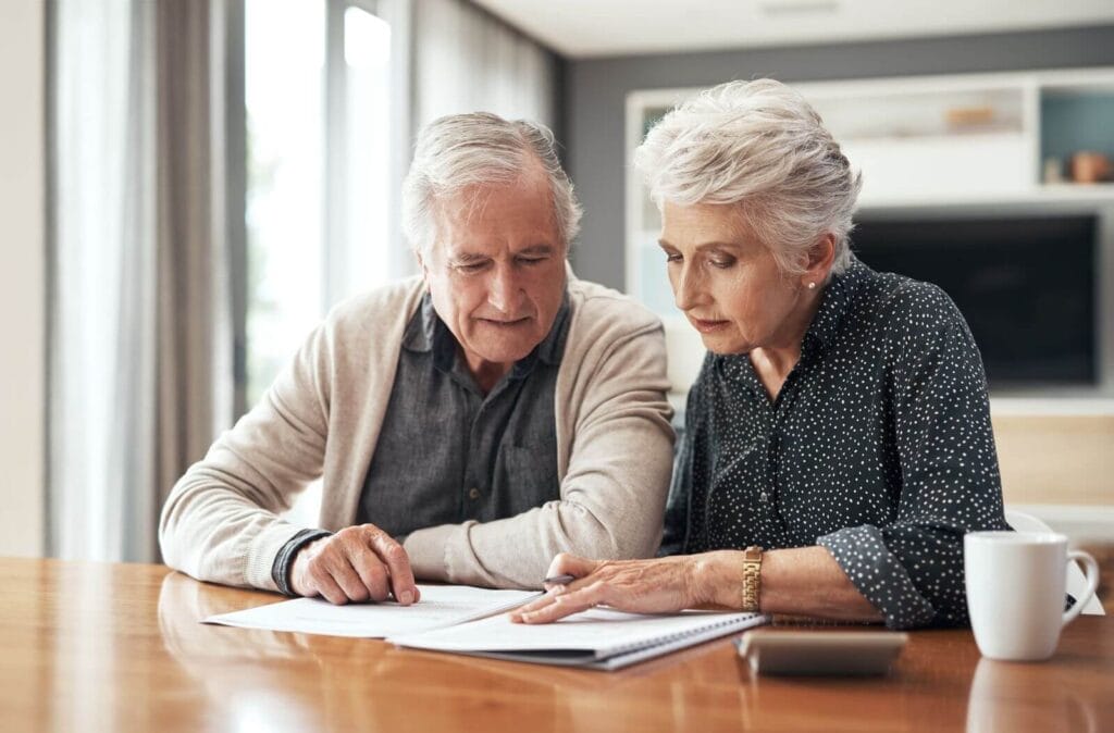 An older adult man and woman sit at a table looking over paperwork.