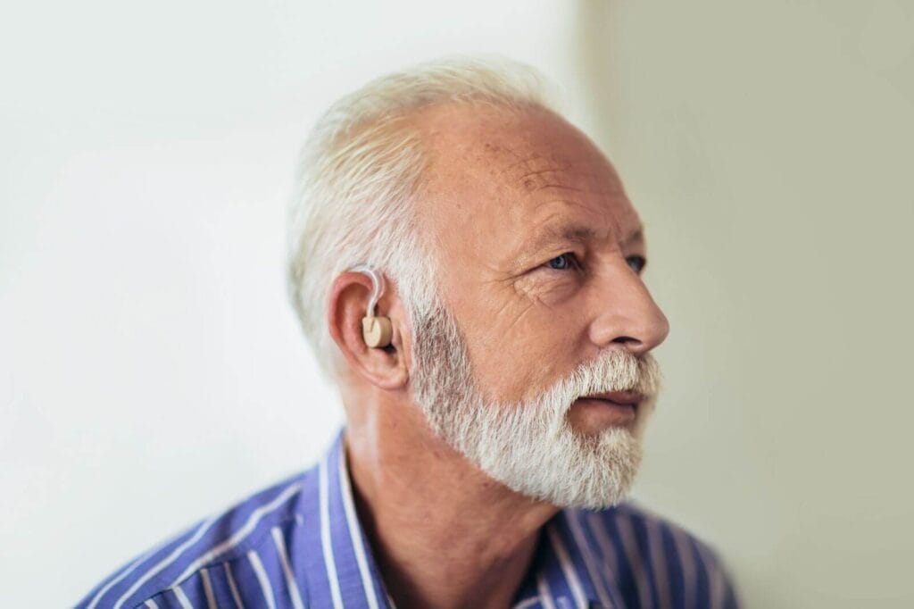 An older adult man is sitting in profile. He has a hearing aid in his ear.