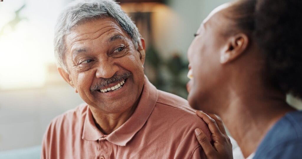 An older adult man wearing a hearing aid smiles at a woman sitting next to him.