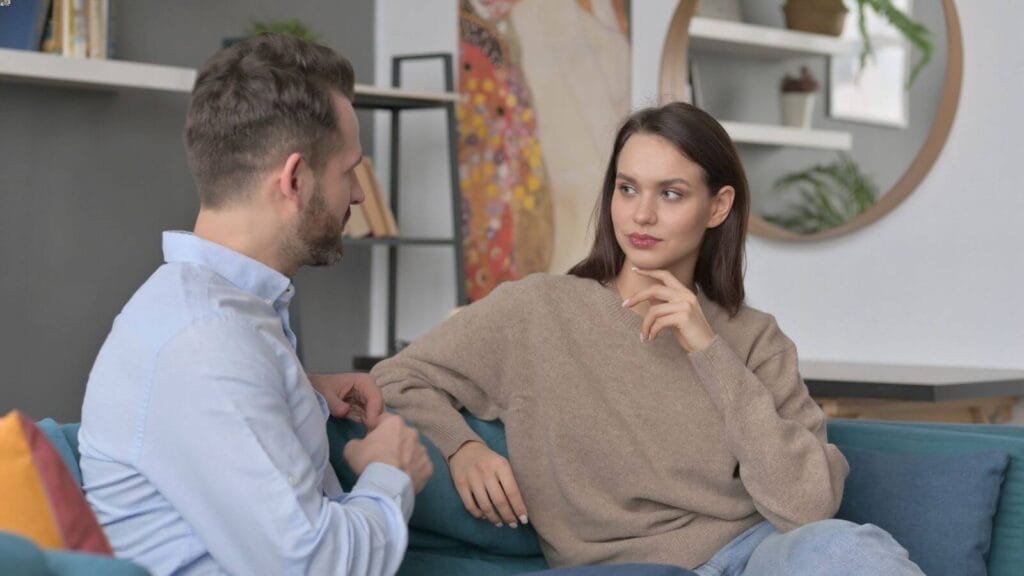 A man and woman sit on a couch, having a discussion.