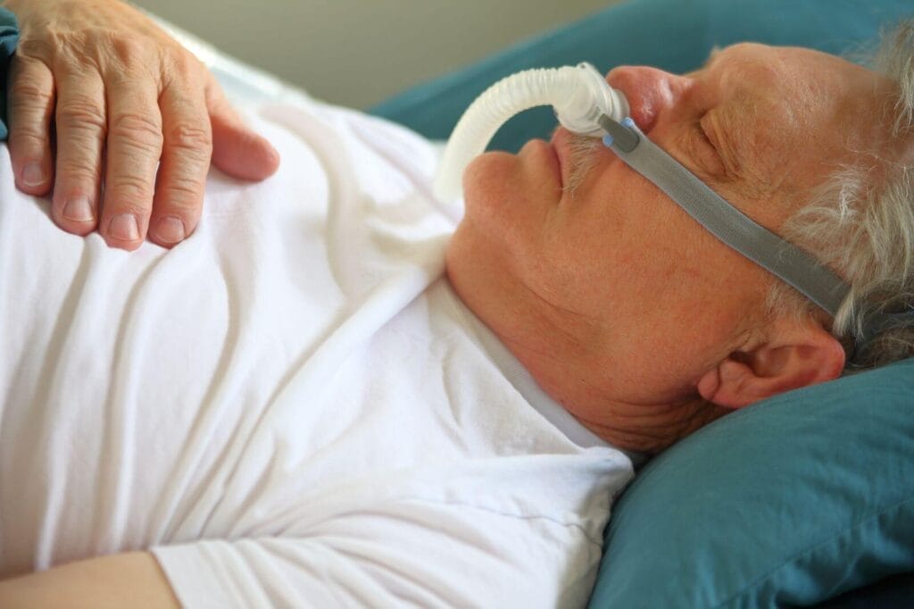 An older adult man sleeps in bed using a cpap machine.