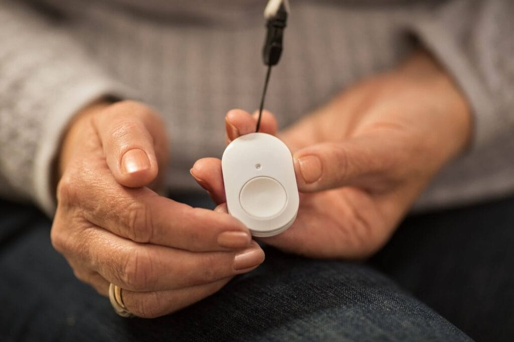 A woman's hands are shown holding a medical alert system emergency pendant.