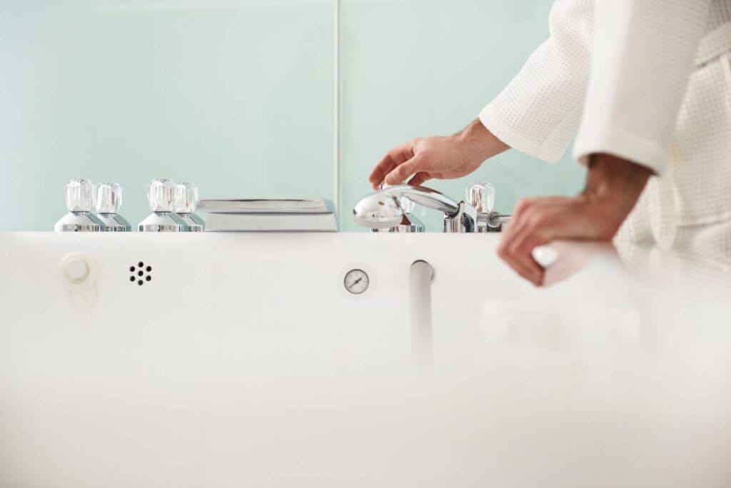 A person's hands are shown turning on the faucet of a bathtub.