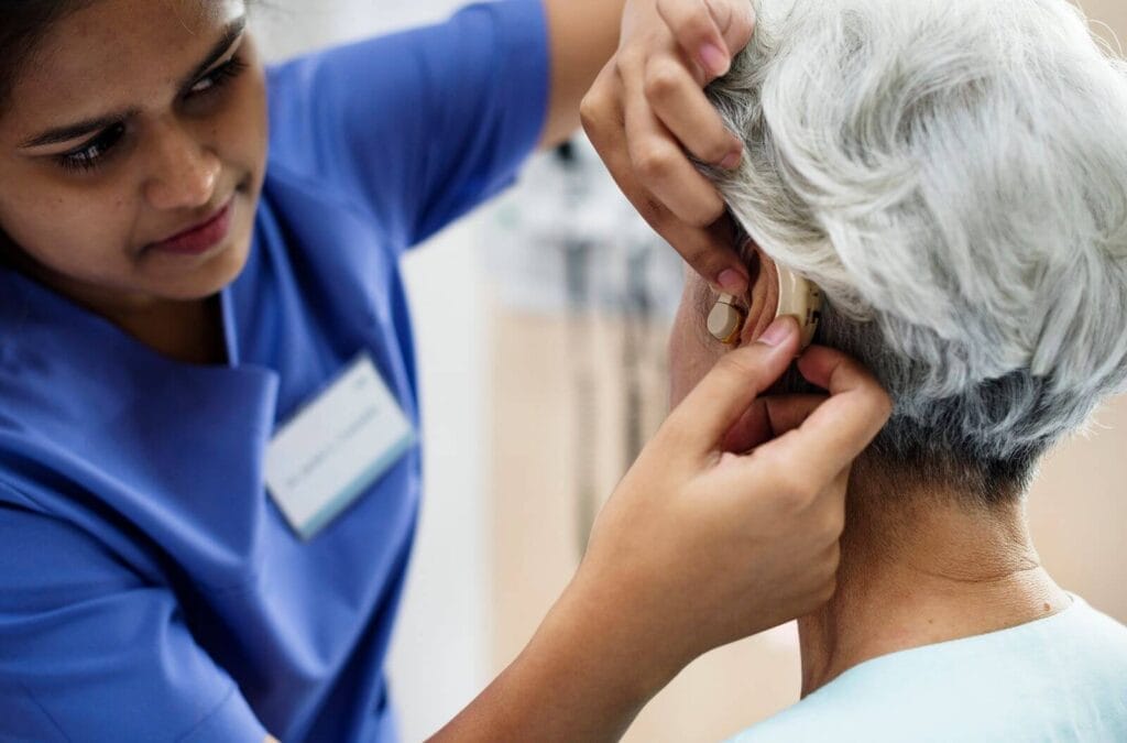 A female doctor places a hearing aid in the ear of an older adult woman.