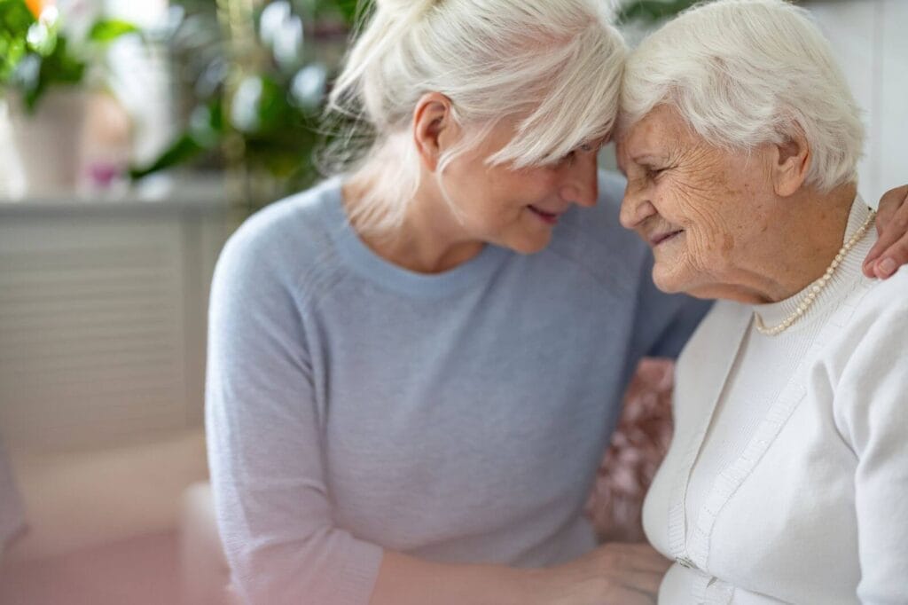 A woman and her older adult mother place their foreheads against each other. They smile.