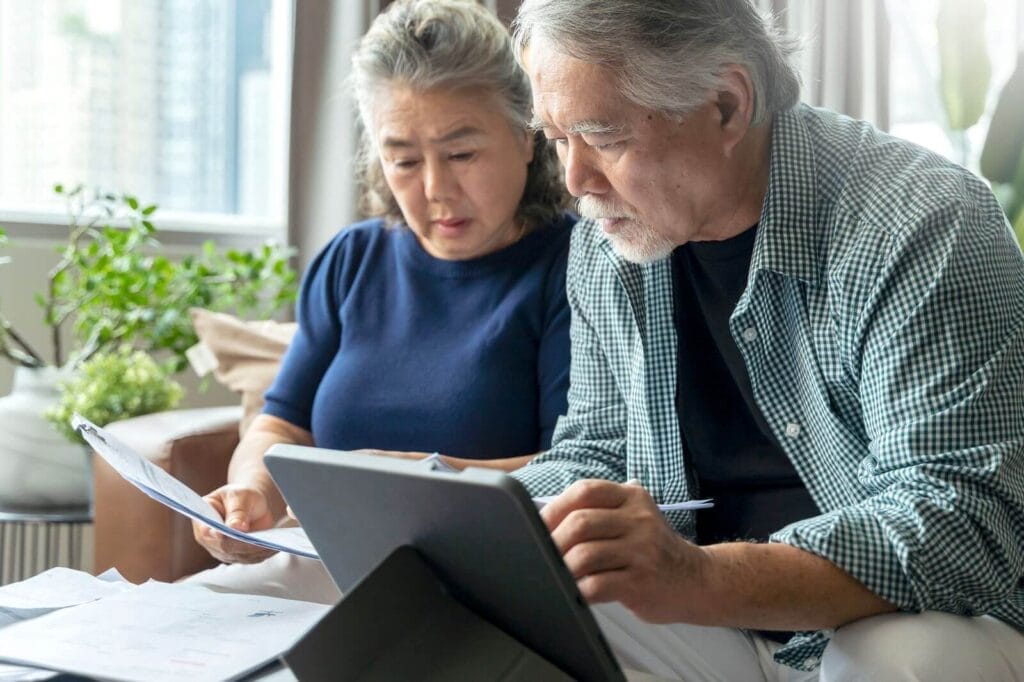 An older adult man and woman sit on a couch looking over paperwork.