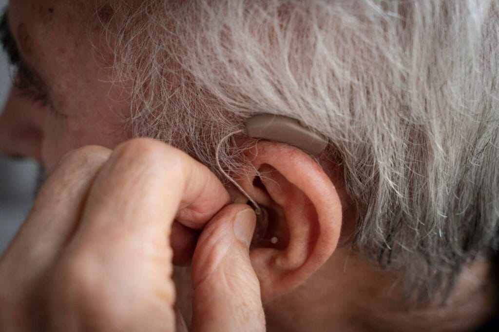 A close-up of an older adult man's ear as he inserts a hearing aid.