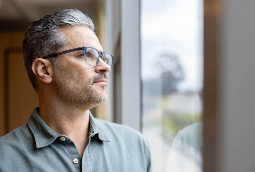 A man looks pensive as he looks out a window.