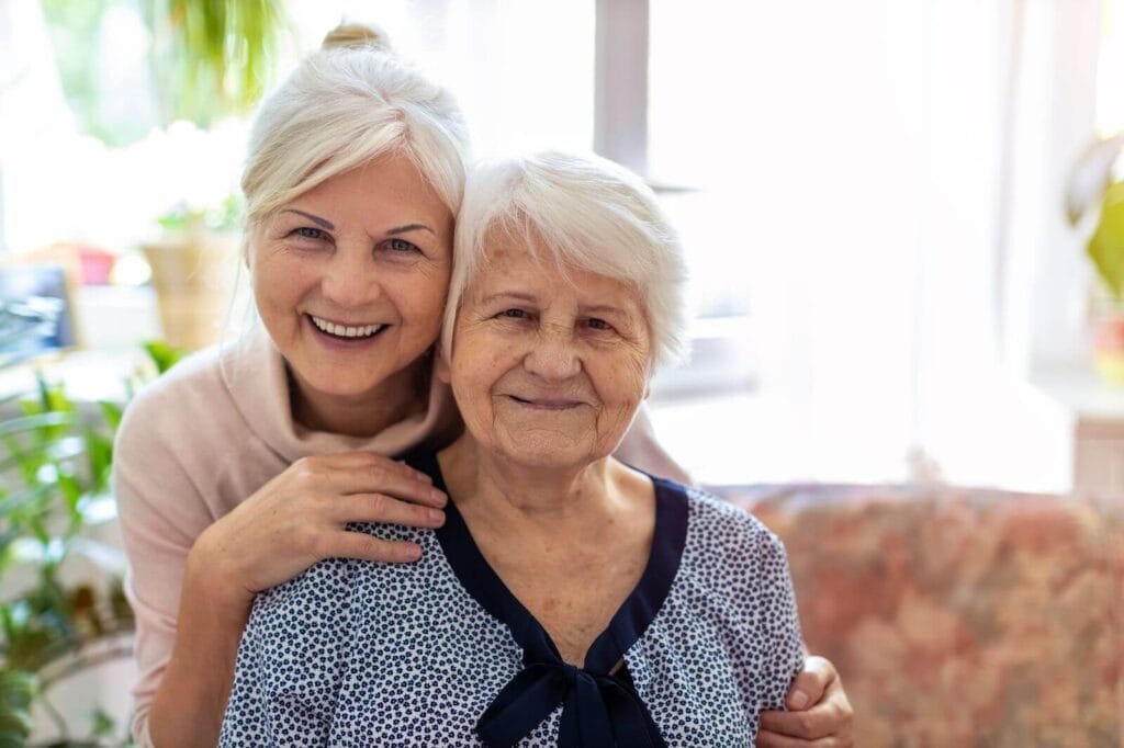 A woman and her older adult mother smile at the camera.