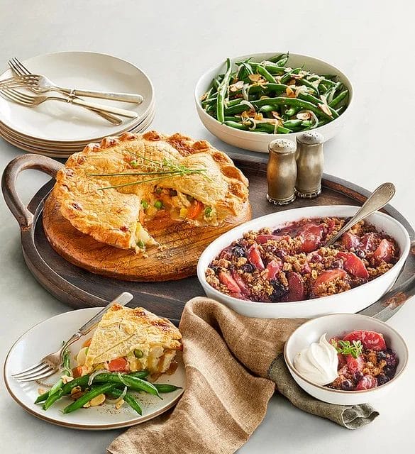 Image of a meal, including a chicken pot pie, green beans with sliced almonds, blueberry peach crisp dessert, plates and forks, and salt and pepper shakers.