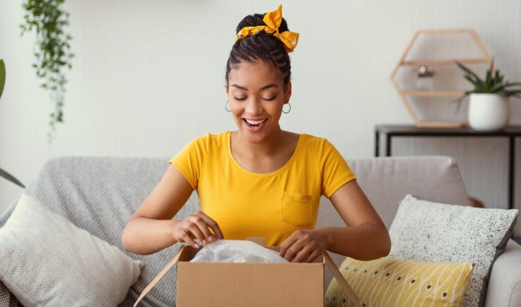 A happy woman sitting on a couch opens a gift.