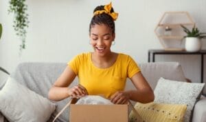 A happy woman sitting on a couch opens a gift.